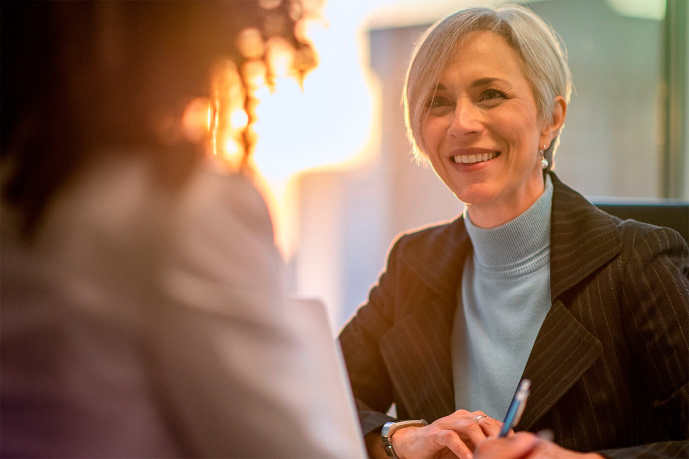 A view over a woman's shoulder showing a smiling businesswoman, possibly engaged in discussions related to escrow services, corporate actions, and corporate escrow support.